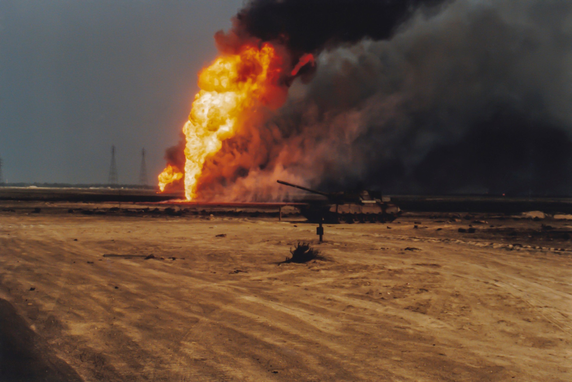 Oil well burning in field with remains of burned tank